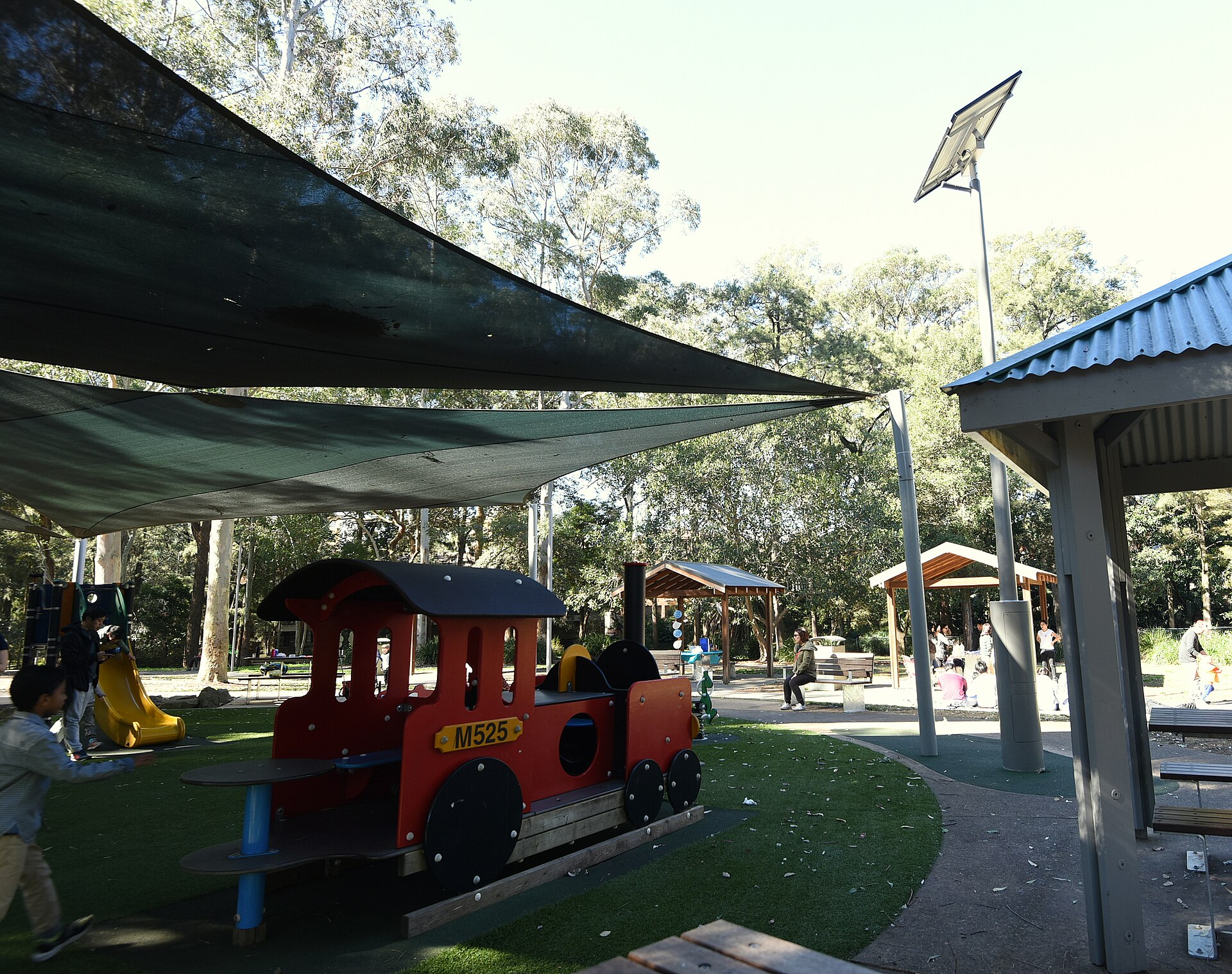 Children's playground with a red toy steam train, shade sails and picnic shelters at Boronia Park, Epping