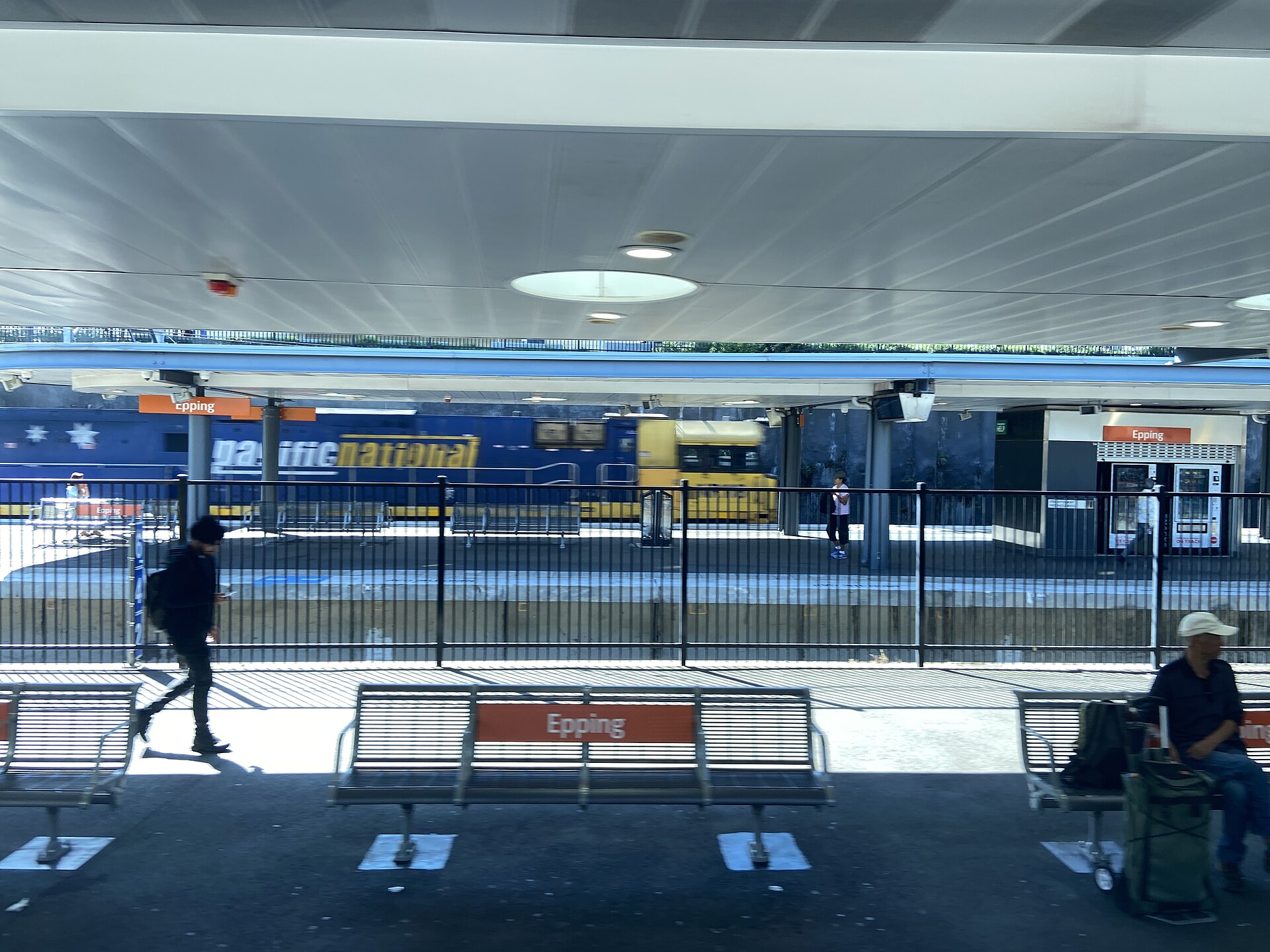 Platform seating at Epping Station with a freight locomotive passing on the next line