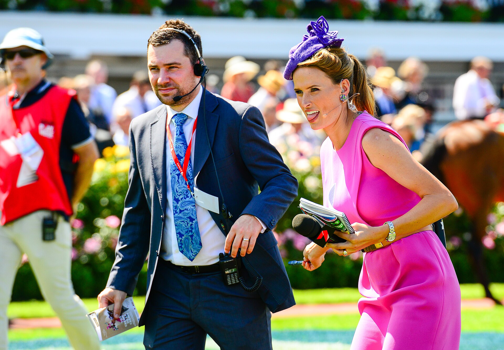 Two broadcasters in a pink dress with a purple fascinator and a navy suit at Flemington's Super Saturday in 2014