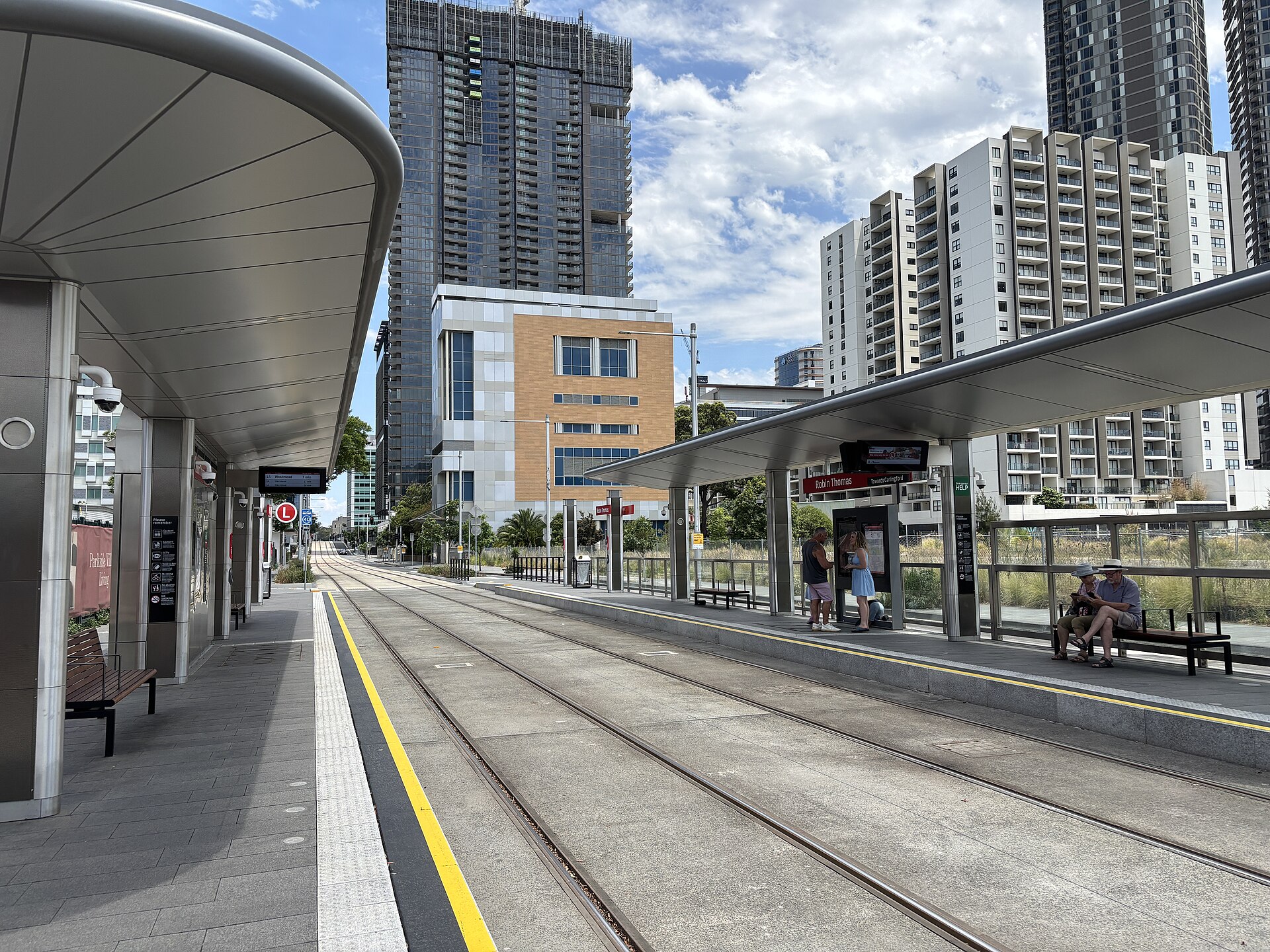 The Robin Thomas light rail stop in Parramatta with a platform shelter, tram tracks and apartment towers