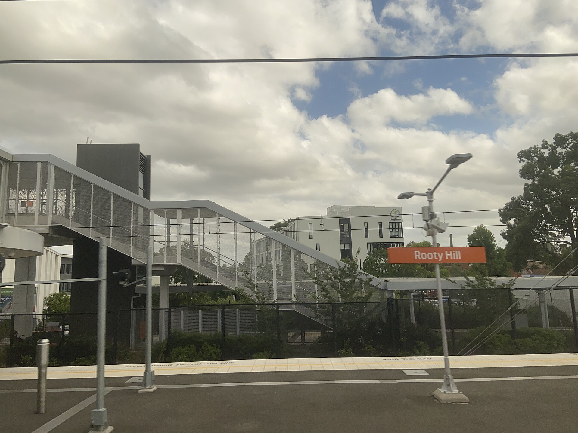 Rooty Hill station platform sign and footbridge, seen from a train window