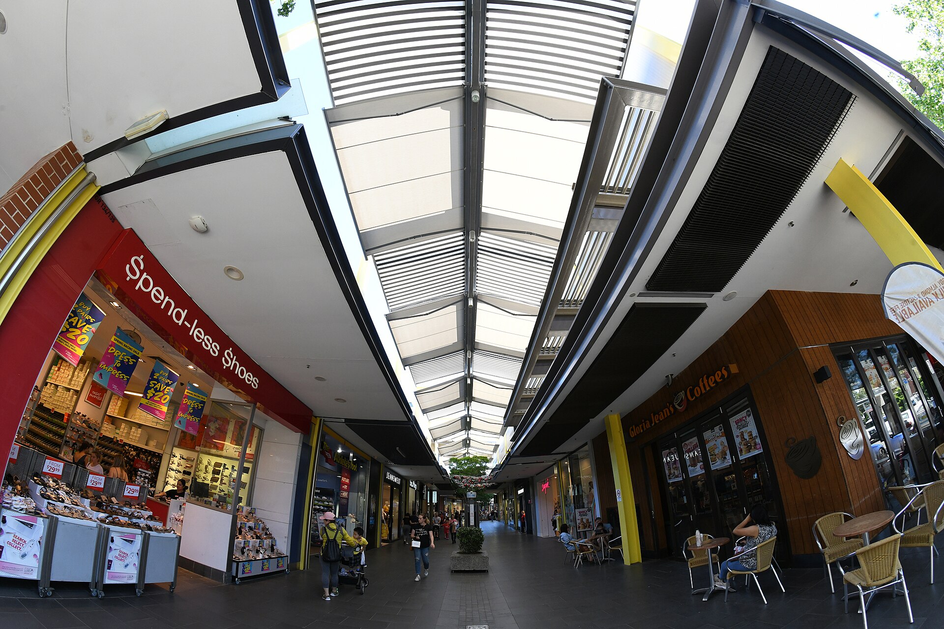 A covered shopping arcade at Rouse Hill Town Centre with a newsagency, a nail salon and a family walking