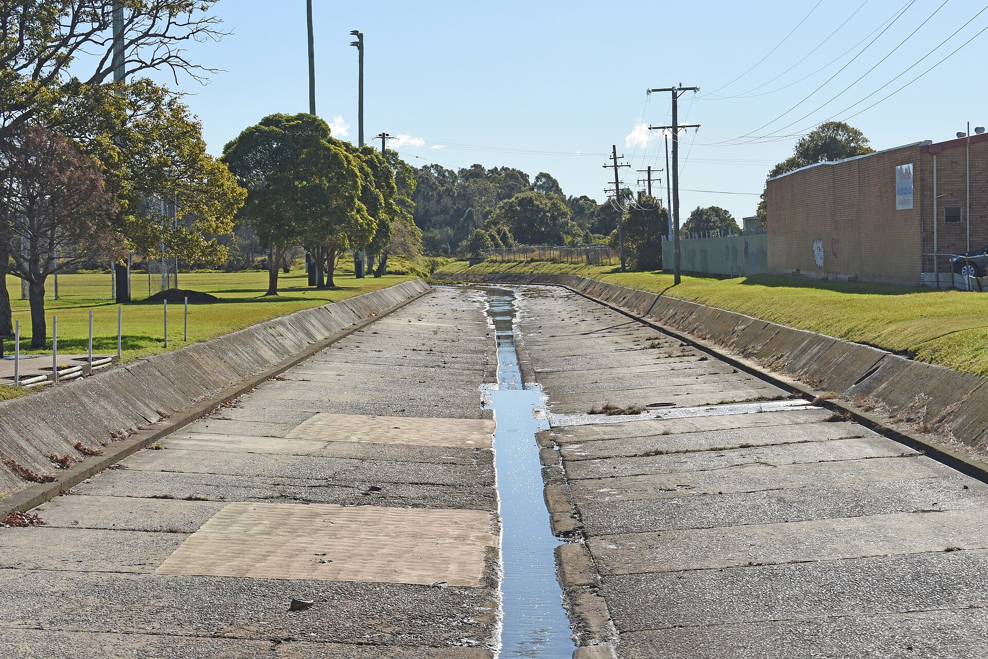 Part of Iron Bark Creek in Wallsend, Newcastle, a concrete channel beside a playing field, 2023